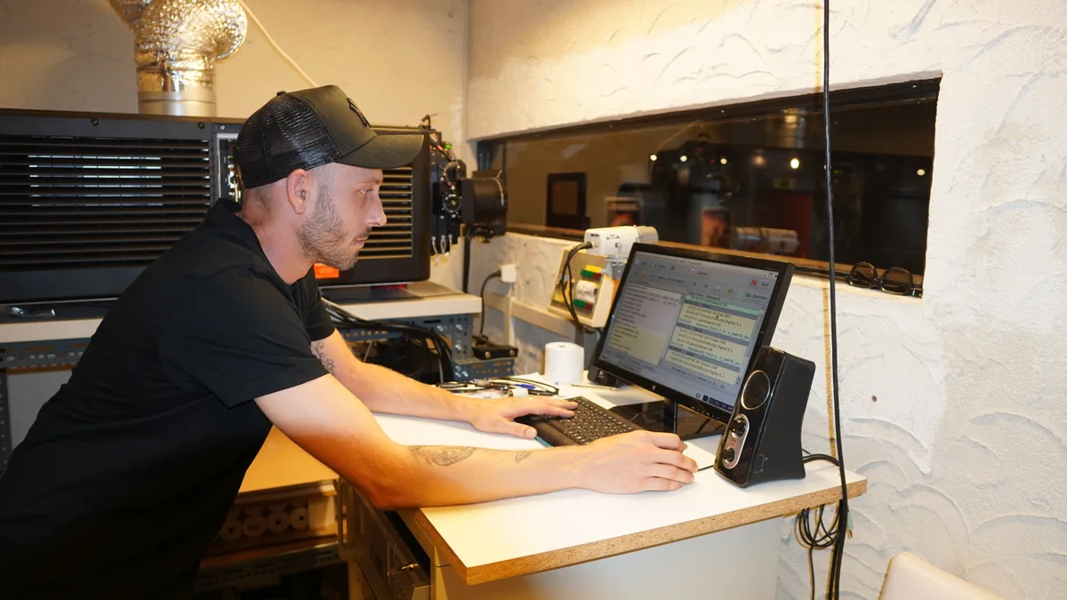 Ein junger Mann mit Baseballmütze sitzt im Projektionsraum eines Kinos.